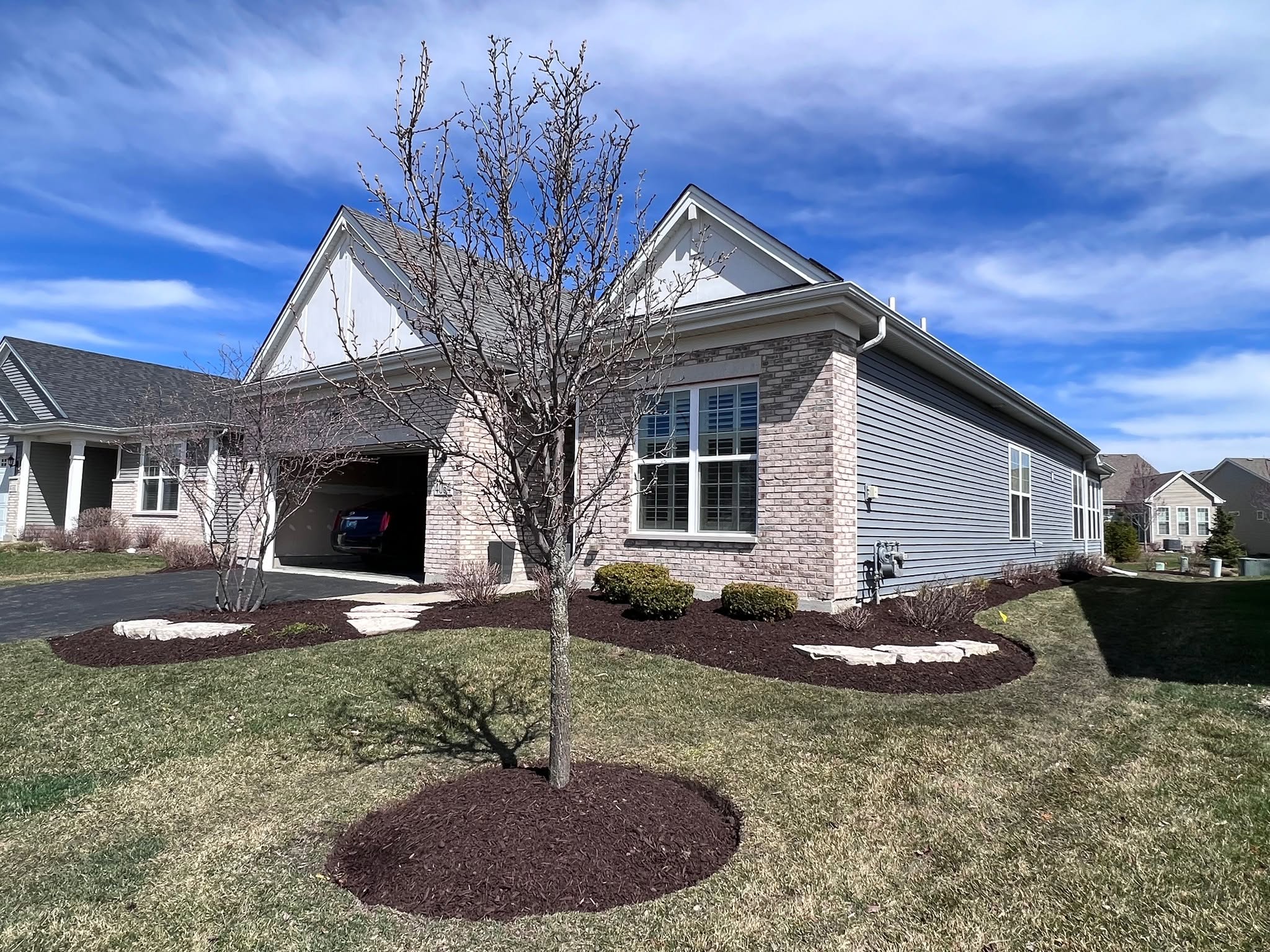Company photo of dark mulch, shrubs, and natural stone accents around a front yard